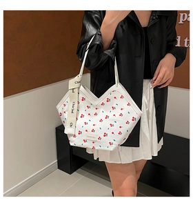 Detail of white tote bag with red cherry print featuring decorative brand ribbon and logo
