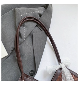 Détail du cabas en cuir marron foncé avec nœud en dentelle blanche et gaufrage
