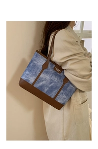 Close-up of blue denim tote bag with brown leather straps and fashion label on model