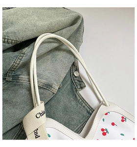 Detail of white tote bag with red cherry prints and stylish lettered webbing strap