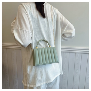 Detail of light green wavy quilted crossbody bag with golden chain and twisted handle
