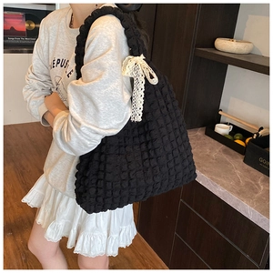Close-up of black tote bag with cloud pleated texture and white lace bow detail