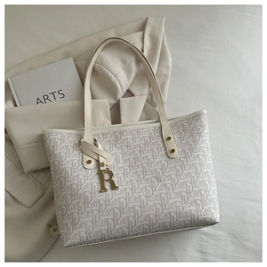 Detail view of cream monogram tote bag featuring gold R-pendant and metal rivets