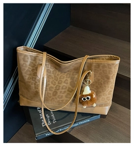 Close-up of leopard print suede tote bag with cute plush pendant on a wooden staircase