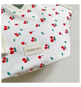 Detailed close-up of cherry pattern canvas bag with fashion leather tag and beige trim