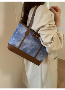 Detailed view of blue washed canvas tote with brown leather trim and fashion brand label