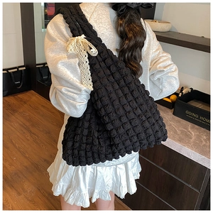 Detail of black bubble texture tote bag featuring a white lace bow on the shoulder strap
