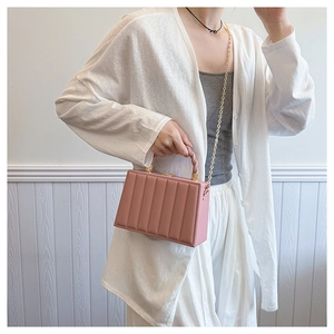 Detail of pink wavy texture crossbody bag with gold chain strap worn by a model
