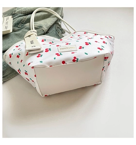 Detail view of large white tote bag featuring red cherry prints and leather strap