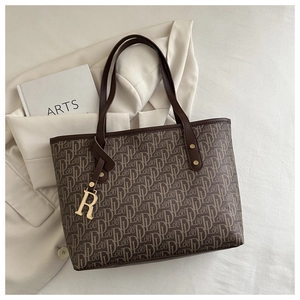 Detail of dark brown tote bag with letter print pattern and gold metal R-pendant