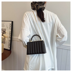 Detail of black wave textured handbag with golden chain strap and woven handle design