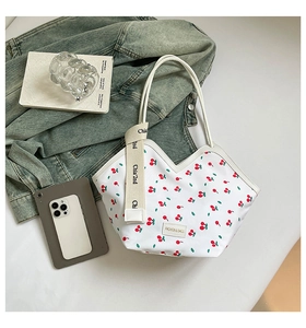 Detail of white tote bag with red cherry print, fabric strap, and logo on clean background