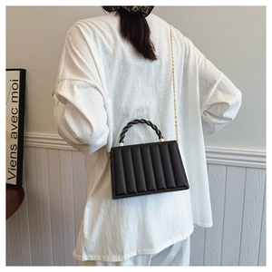 Close-up of black quilted crossbody bag featuring woven handle and gold chain strap