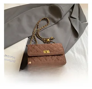 Detail of brown quilted suede handbag showing golden turn-lock and chain strap