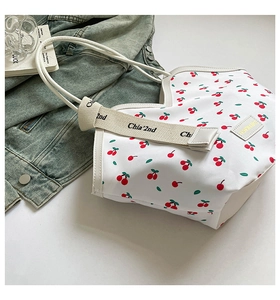 Detail of white tote bag with red cherry print and decorative branded woven straps