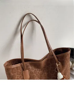 Detail of leopard print tote bag featuring smooth brown straps and a white knit hat charm