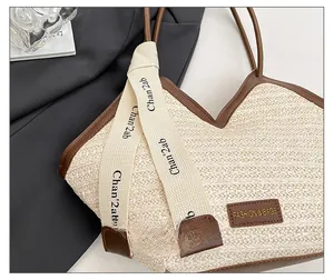 Detail of beige straw tote bag featuring leather logo patch and decorative ribbon strap