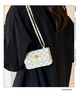 Model wearing a white monogram crossbody bag with gold buckle and leather-chain strap