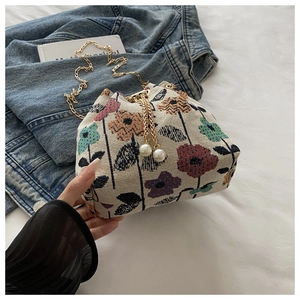 Detailed shot of ethnic floral bucket bag with pearl charms and gold chain strap