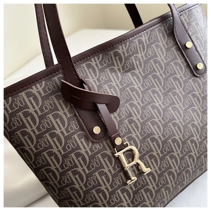 Close-up of monogram jacquard fabric with brown leather handles and gold R pendant