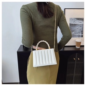 Detail of white quilted handbag with woven gold handle and slim metallic chain strap