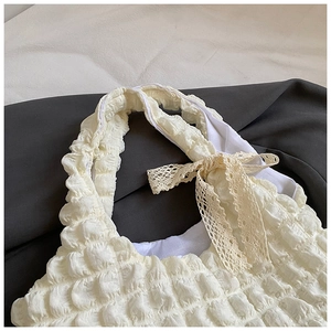 Détail du sac en tissu popcorn crème avec un nœud en dentelle délicat sur la bandoulière