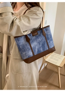 Detail of blue denim tote bag with brown leather handles and rectangular logo patch