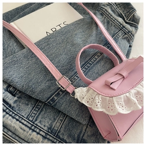Close-up of pink mini crossbody bag with leather bow and white lace detail on denim