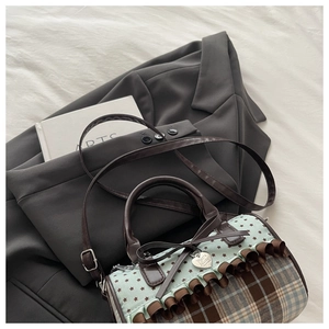 Detail of Boston bag showing plaid fabric, leather bow, and heart metal pendant