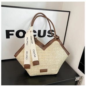Close-up of woven straw tote bag featuring brown faux leather trim and ribbon handle detail