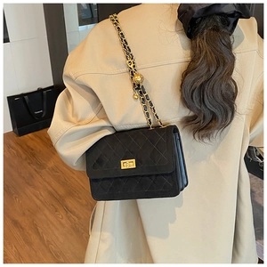 Close-up of black quilted suede shoulder bag featuring a gold chain and ball charm detail
