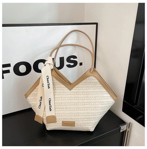 Close-up of woven straw tote bag with leather handles and decorative ribbon detail