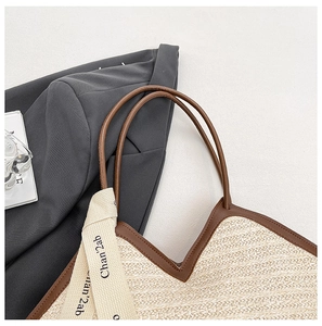 Detail view of woven straw tote bag with brown leather handles and decorative ribbon