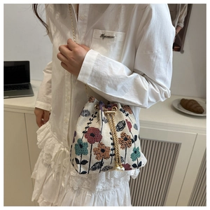 Close-up of cream floral embroidered bucket bag with gold chain strap on a model