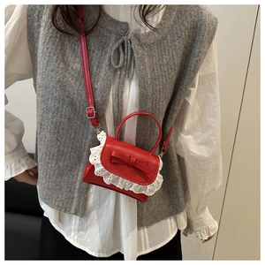 Detail of red mini crossbody bag featuring white lace trim and bow accent on model