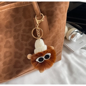 Detail of plush pompom charm with sunglasses and knit hat on leopard tote bag