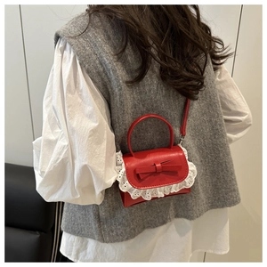 Close-up of a mini red leather crossbody bag with a bow and white lace trim detail