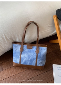 Close-up of vintage denim tote bag with brown leather handles and stitched logo