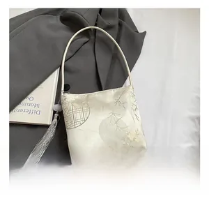 Detalle del bolso tipo saco de seda crema con bordado chino y borla de perlas