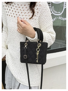 Detail of black quilted crossbody bag featuring a gold key charm and fine shoulder strap