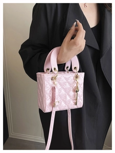 Detail of pink quilted handbag with gold key charm and cylindrical dual handles