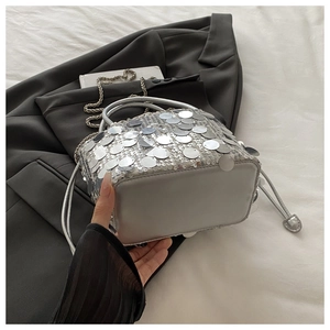 Detailed view of silver sequin bucket bag with metal chain strap on fabric background