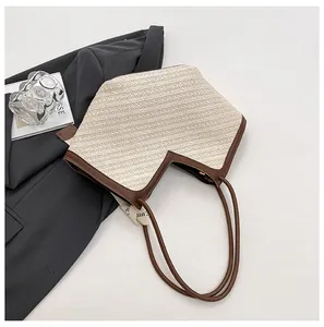 Detail of straw tote bag featuring V-shaped opening and brown leather shoulder straps
