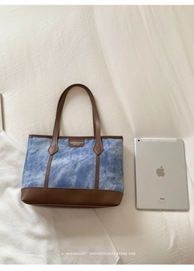 Top view of blue denim tote bag with brown leather trim next to an iPad for size reference