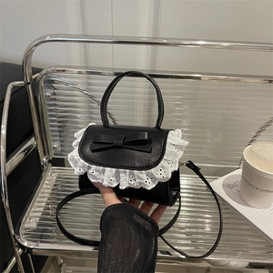 Mini black leather crossbody bag with white lace ruffles and bow in a stylish setting