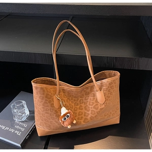 Close-up of leopard print tote bag with brown plush monster keychain and slim shoulder straps
