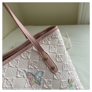 Détail du motif papillon brodé sur un sac cabas matelassé avec anse en cuir rose
