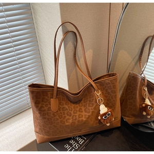 Detail of leopard print tote bag with plush charm and suede stitching in a cozy setting