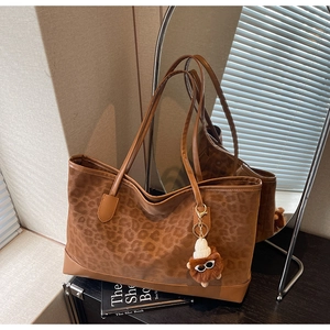 Detail of leopard print tote bag with brown corners and a cute monster charm accessory