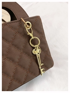 Close-up of brown quilted leather bag featuring a vintage gold key charm and fine stitching